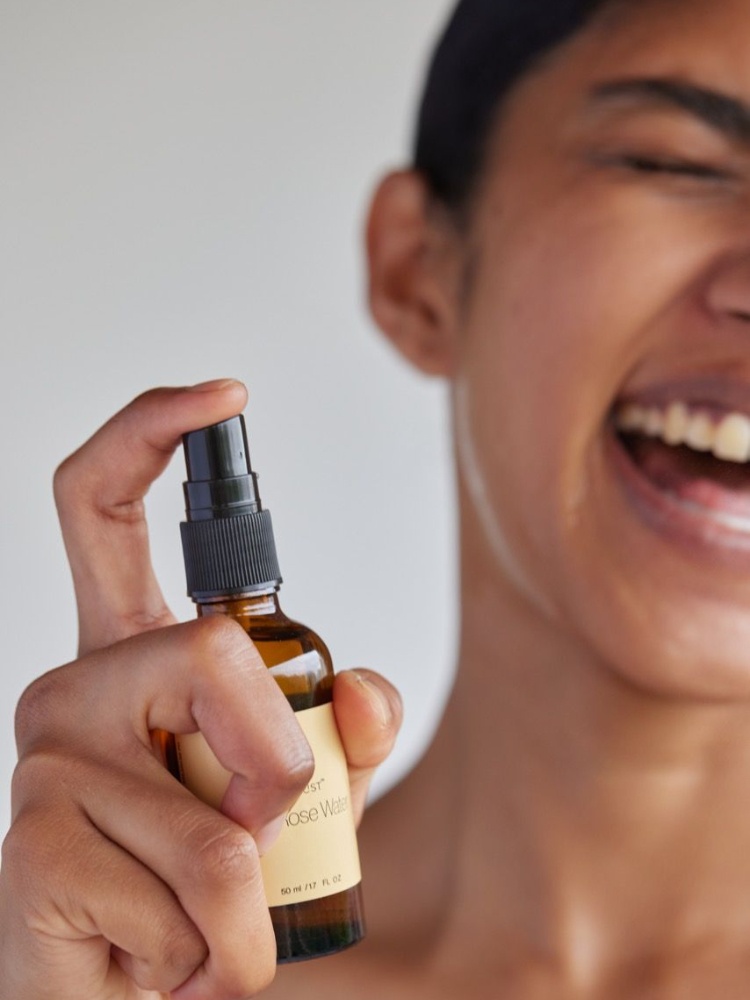 A woman sprays rose water on her face